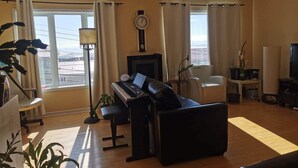 A living room with a piano, a sofa, a television, and a view of the city. - Grant's Arctic Escape (Iqaluit)