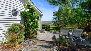 A house with a wooden deck, a small garden, and a view of the landscape. - Oyster Catcher | Deep Creek Waterfront w/ Deep Water Dock, Screened Porch, Guest Cottage & Pets (Chincoteague Island)