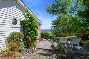 A house with a wooden deck, a small garden, and a view of the landscape. - Oyster Catcher | Deep Creek Waterfront w/ Deep Water Dock, Screened Porch, Guest Cottage & Pets (Chincoteague Island)
