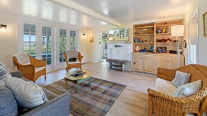 A spacious living room with wicker furniture, a fireplace, and a view through large glass doors. - Oyster Catcher | Deep Creek Waterfront w/ Deep Water Dock, Screened Porch, Guest Cottage & Pets (Chincoteague Island)