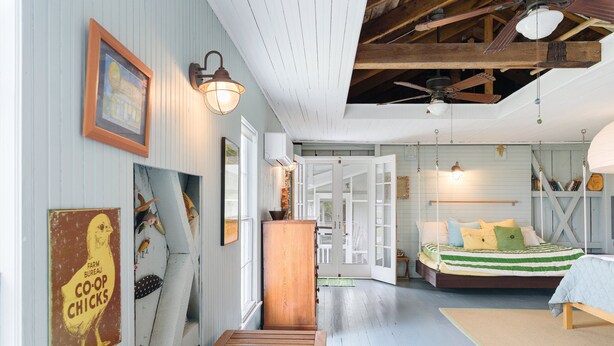 A room with a bed, wooden floor, and a staircase leading to another room. - Oyster Catcher | Deep Creek Waterfront w/ Deep Water Dock, Screened Porch, Guest Cottage & Pets (Chincoteague Island)
