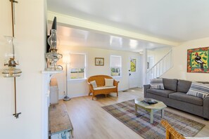 A living room with a sofa, a coffee table, a wicker chair, and a patterned rug. - Oyster Catcher | Deep Creek Waterfront w/ Deep Water Dock, Screened Porch, Guest Cottage & Pets (Chincoteague Island)