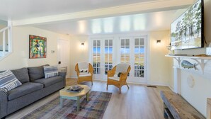 A living room with a sofa, two chairs, a coffee table, and a TV. - Oyster Catcher | Deep Creek Waterfront w/ Deep Water Dock, Screened Porch, Guest Cottage & Pets (Chincoteague Island)