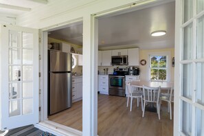 A kitchen with white cabinets, stainless steel appliances, and a dining area with white chairs. - Oyster Catcher | Deep Creek Waterfront w/ Deep Water Dock, Screened Porch, Guest Cottage & Pets (Chincoteague Island)