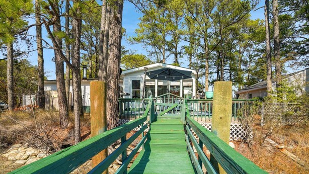 A wooden bridge leading to a white building with a covered porch, surrounded by trees. - Counting Corks | Waterfront Pet Friendly Cottage w/ Dock for Crabbing, Firepit & Near Cape Charles (Cape Charles)