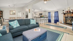 A spacious living room with a sofa, ottoman, and a dining area with a table and chairs. - Counting Corks | Waterfront Pet Friendly Cottage w/ Dock for Crabbing, Firepit & Near Cape Charles (Cape Charles)
