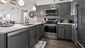 A modern kitchen with grey cabinets, stainless steel appliances, and a wooden floor. - Chic & charming 2 bedroom oceanfront condo w/amazing views & large pool! (North Myrtle Beach)