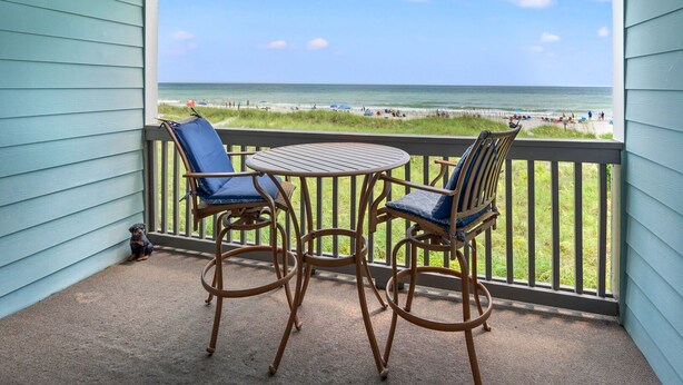 A balcony with two chairs and a table, overlooking a beach with people and umbrellas. - Chic & charming 2 bedroom oceanfront condo w/amazing views & large pool! (North Myrtle Beach)