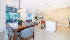 Uma cozinha moderna com uma ilha central, uma sala de jantar com mesa e cadeiras de madeira, e uma sala de estar com sofá e televisão.