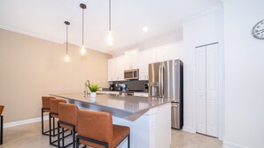 Cozinha moderna com ilha central, eletrodomésticos de aço inoxidável e iluminação pendente.