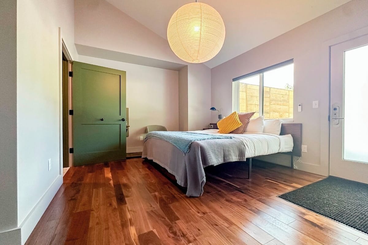A bedroom with a bed, a green door, a large window, and a hanging light fixture.
