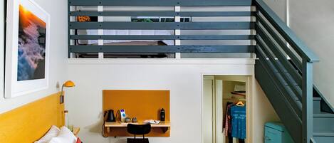 A room with a bunk bed, a desk with a chair, a wardrobe, and a small fridge.