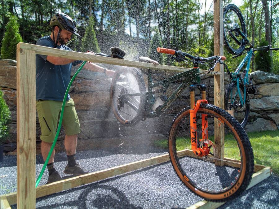 A person cleaning a bicycle in a wooden frame structure outdoors.