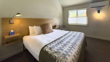 A bedroom with a bed, a nightstand, a lamp, a chair, a window, and an air conditioning unit.
