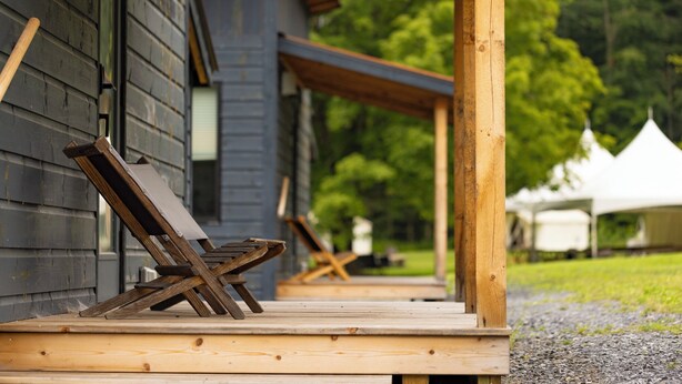 A wooden deck with a bench and a table, leading to a building with a dark exterior. - Madbush Falls (Waitsfield)