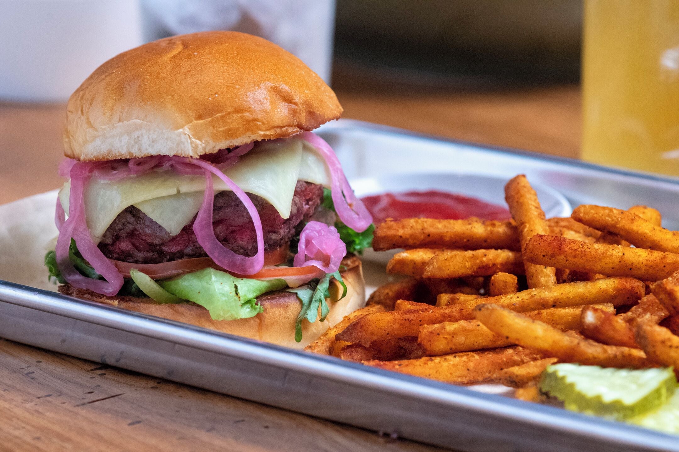 A burger with fries and a pickle on a tray.
