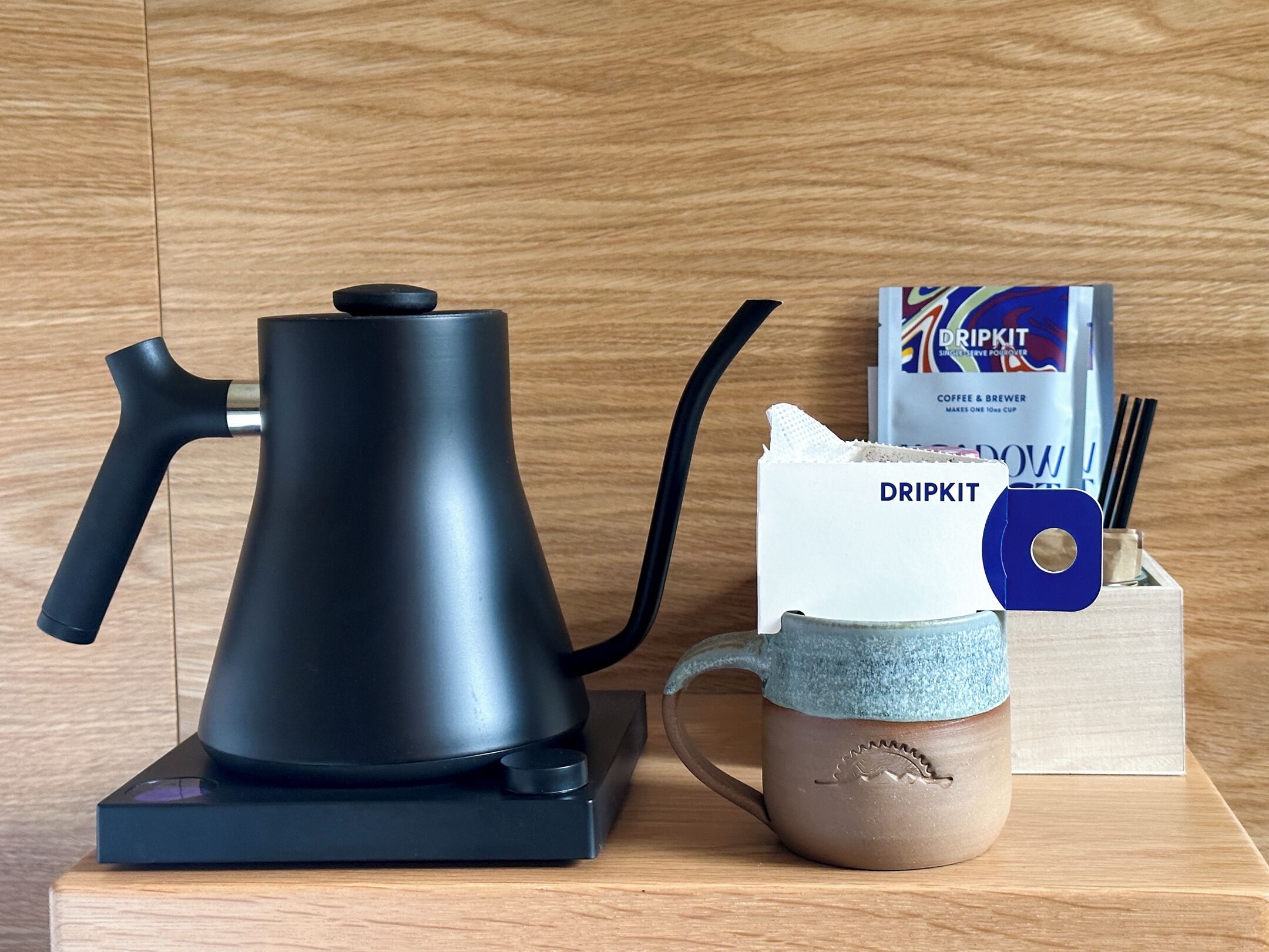 Een zwarte elektrische waterkoker, een koffiezetapparaat en een mok op een houten ondergrond.