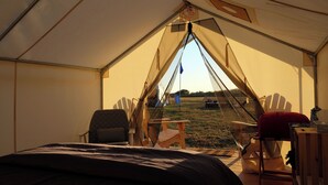 A tent with a bed, two chairs, a table, and a view of a grassy field. - Madbush Falls (Waitsfield)