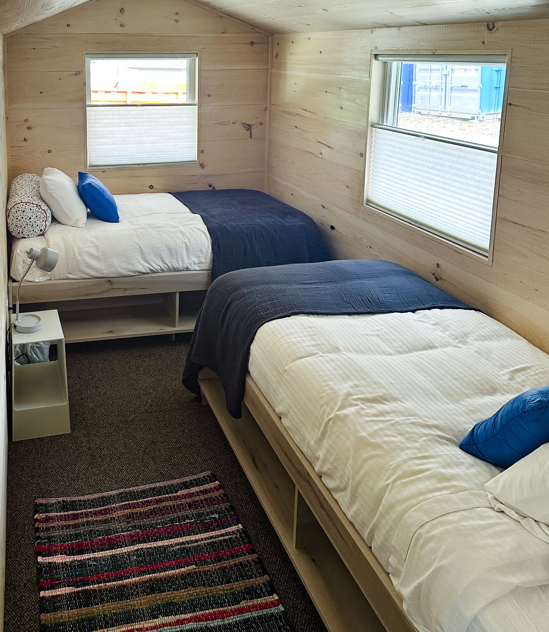 Et lille træværelse med to senge, et lille bord og et vindue.