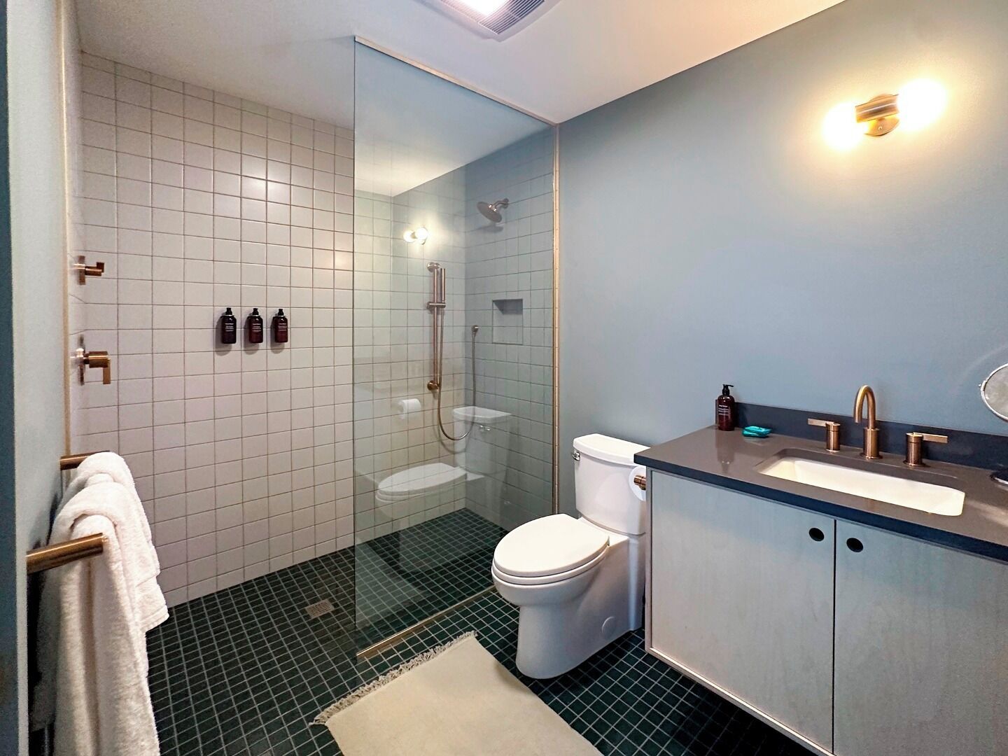Un baño moderno con ducha envuelta en vidrio, inodoro blanco y tocador con lavamanos y espejo.