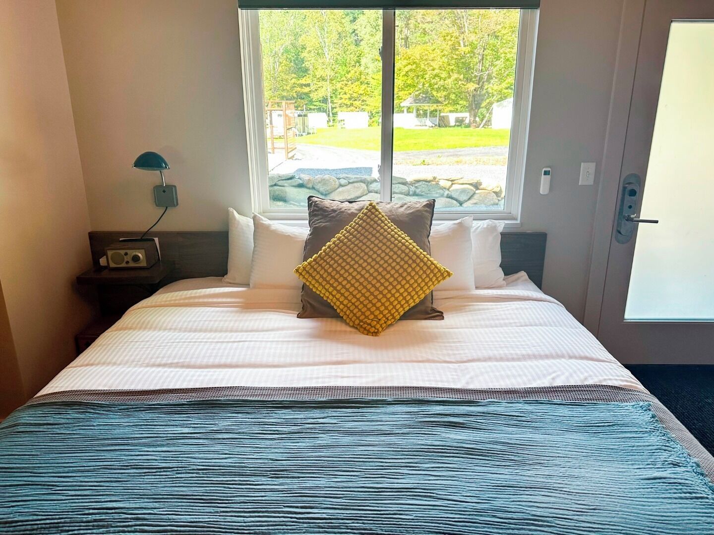 Ein Hotelzimmer mit Bett, einem Fenster mit Parkblick, einem Nachttisch mit Radio und einer Tür mit Griff.