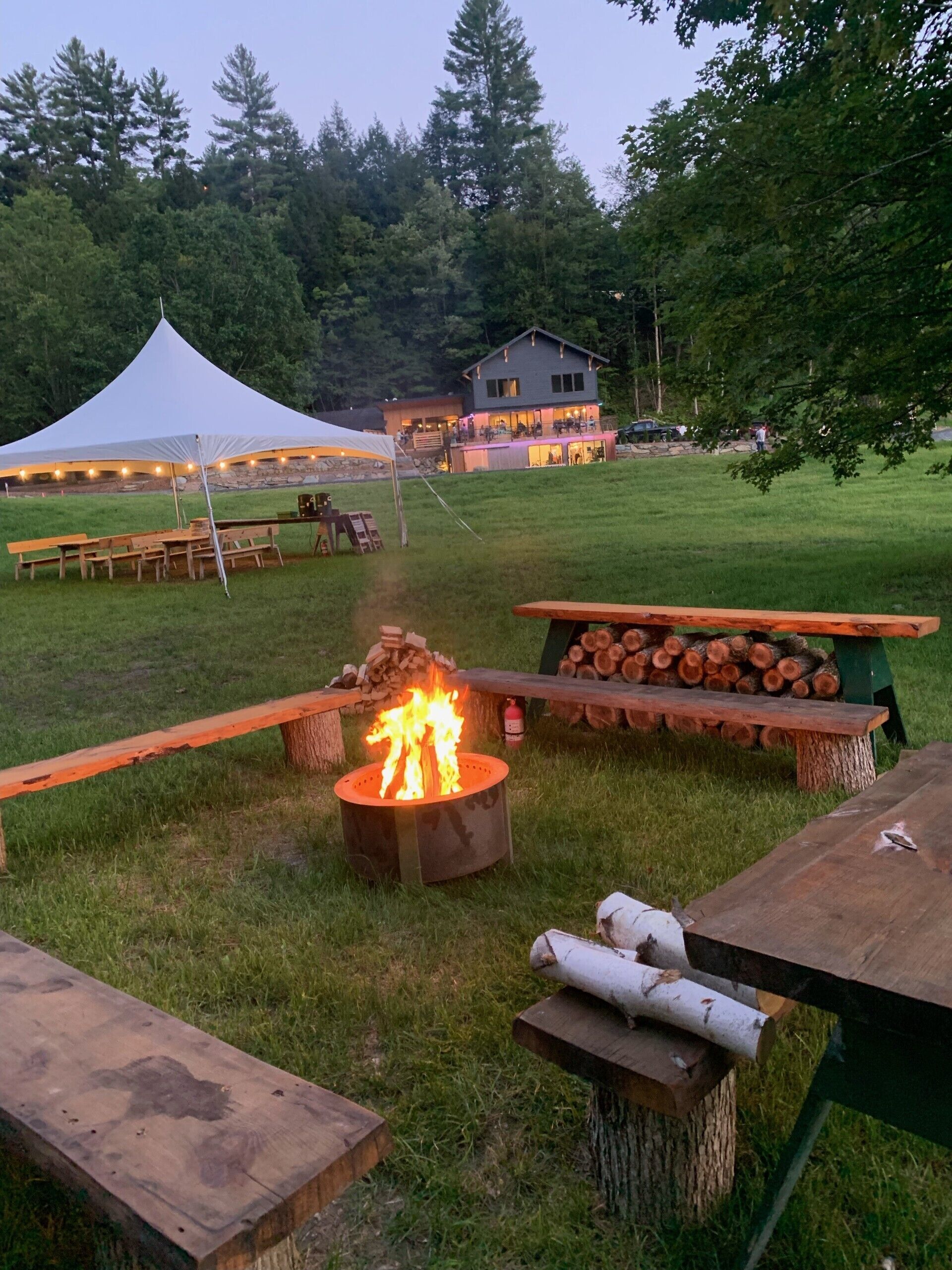Ein Campingplatz im Freien mit Feuerstelle, Picknicktischen und einem Zelt.