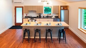 A modern kitchen with a central island, bar stools, and a view of the outdoors. - Madbush Falls (Waitsfield)