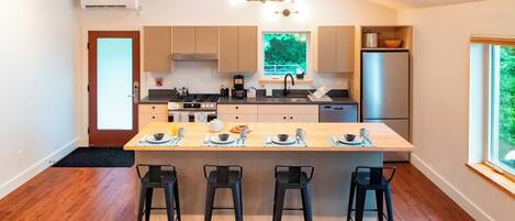 Une cuisine moderne dotée d’un îlot central, de tabourets de bar et offrant une vue sur l’extérieur.