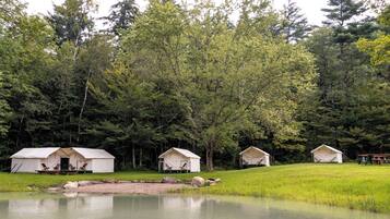A campsite with three tents and a picnic table by a lake, surrounded by dense forest.