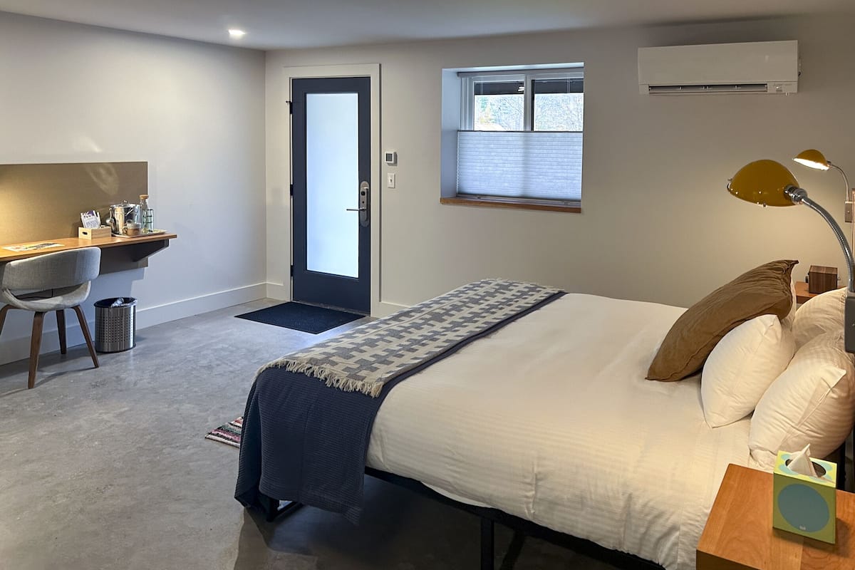 A bedroom with a bed, bedside table, lamp, chair, desk, and window.