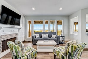 A living room with a fireplace, a large TV, a grey sofa, and striped armchairs. - New Listing! Stunning Oceanfront 4-bedroom 3 bath house nestled on the quiet end of the island. (Fernandina Beach)