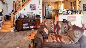 A spacious living area with a wooden staircase, a sofa with patterned cushions, and a kitchen in the background.