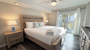 A bedroom with a wooden bed, two bedside tables with lamps, a ceiling fan, and a balcony with a view of palm trees. - El Matador 125 -  FREE TICKETS!! Your stay includes free tickets to many area attractions! (Fort Walton Beach)