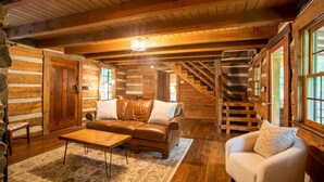 A log cabin interior with a wooden staircase, leather sofa, and a white armchair. - Charming Cabin Near Blue Ridge Mountains (Blowing Rock)