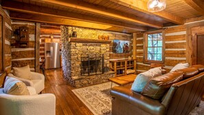 A cozy log cabin interior with a stone fireplace, wooden furniture, and a television. - Charming Cabin Near Blue Ridge Mountains (Blowing Rock)