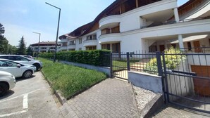 A multi-story residential building with balconies, a paved driveway, and a parking area with cars. - Holiday apartment with air conditioning, in the pedestrian zone (Balatonlelle)