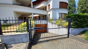 A two-story house with a gated entrance, a covered porch, and a landscaped garden. - Holiday apartment with air conditioning, in the pedestrian zone (Balatonlelle)