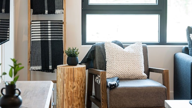 Una habitación acogedora con una silla de madera, un taburete pequeño de madera y una ventana con persianas.