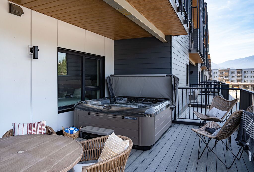 A balcony with a hot tub, wicker chairs, and a wooden table.