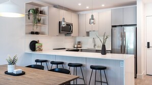 Una cocina moderna con una isla central, taburetes de bar, iluminación colgante y electrodomésticos integrados.