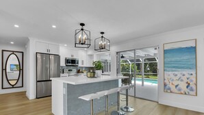 A modern kitchen with a central island, stainless steel appliances, and pendant lighting. - Aqua Cottage- Newly renovated Park Shore home! (Naples)