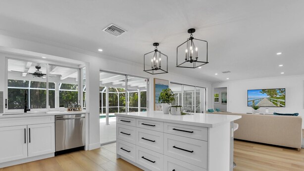 A modern kitchen with white cabinetry, a central island with drawers, and pendant lighting. - Aqua Cottage- Newly renovated Park Shore home! (Naples)