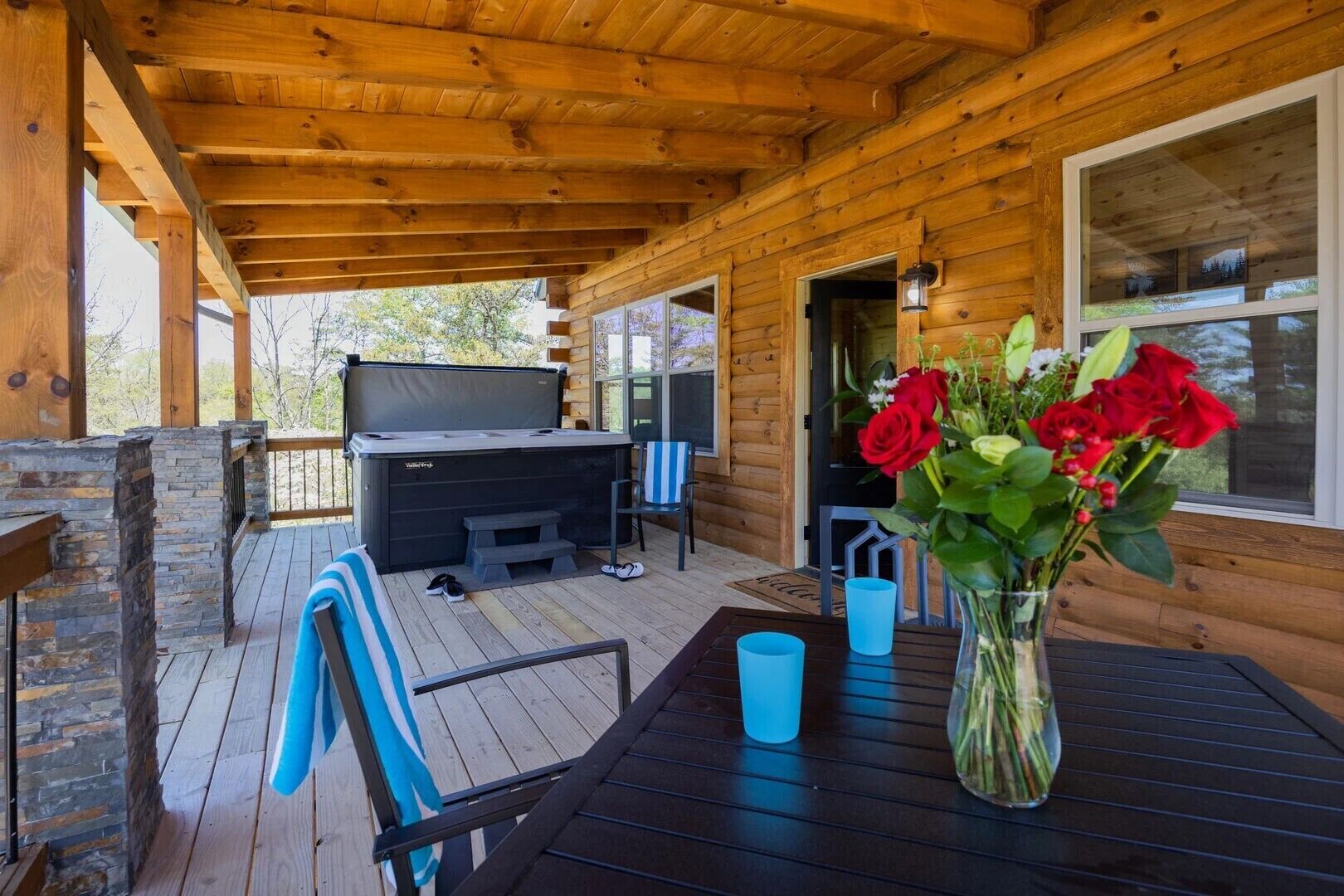 A wooden deck with a hot tub, a table with a vase of flowers, and a TV.