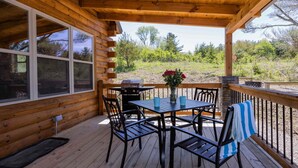 A wooden deck with a table and chairs, a barbecue grill, and a vase with flowers. - Bourbon Trail Lodge by The Inn & Spa at Cedar Falls (Logan)