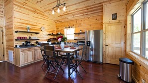 A wooden cabin interior with a dining area, kitchen, and large windows. - Bourbon Trail Lodge by The Inn & Spa at Cedar Falls (Logan)