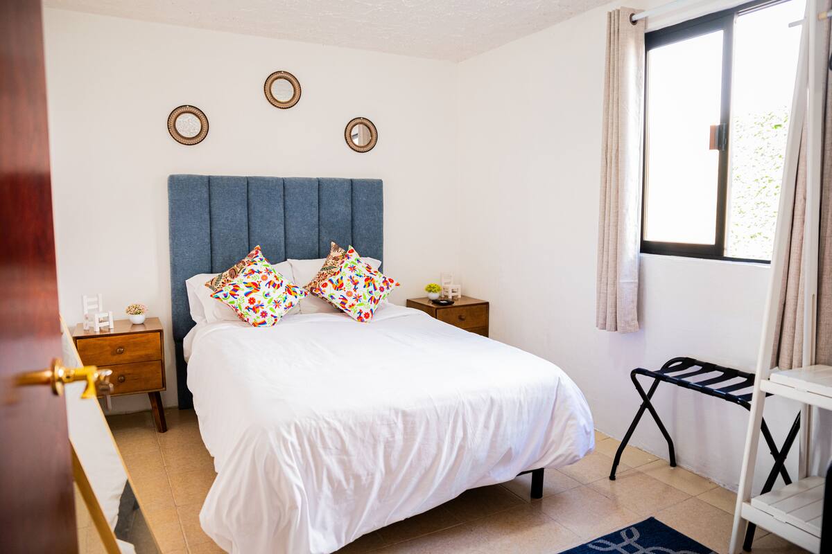 A bedroom with a bed, bedside tables, a window with curtains, and wall decorations.