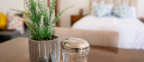 A room with a bed, a bedside table with a potted plant and a salt shaker, and a woven placemat.
