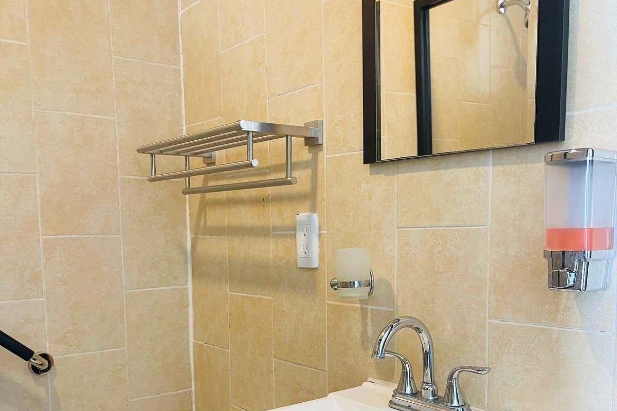 A bathroom with a white toilet, a sink with a black cabinet, a towel rack, a mirror, and a soap dispenser.