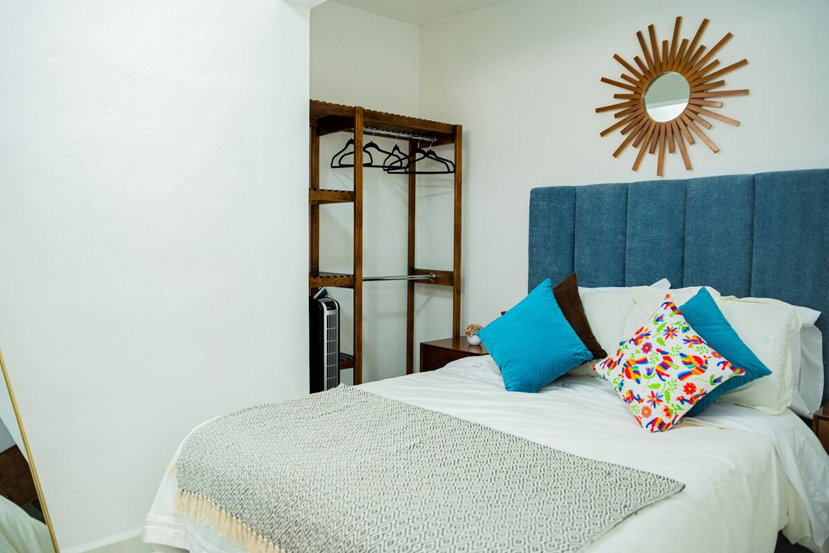 A bedroom with a bed, a blue headboard, a mirror, and a wooden wardrobe.