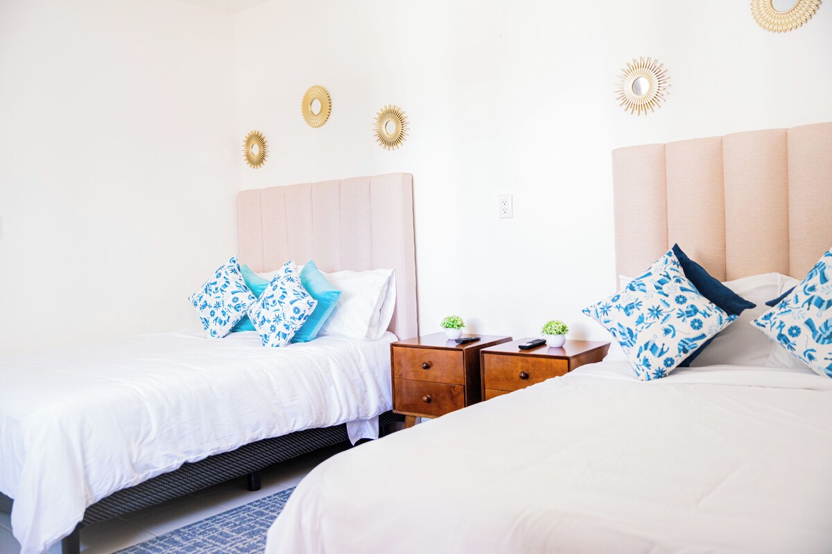 A hotel room with two beds, each with a headboard, and a nightstand with a plant and a remote control.